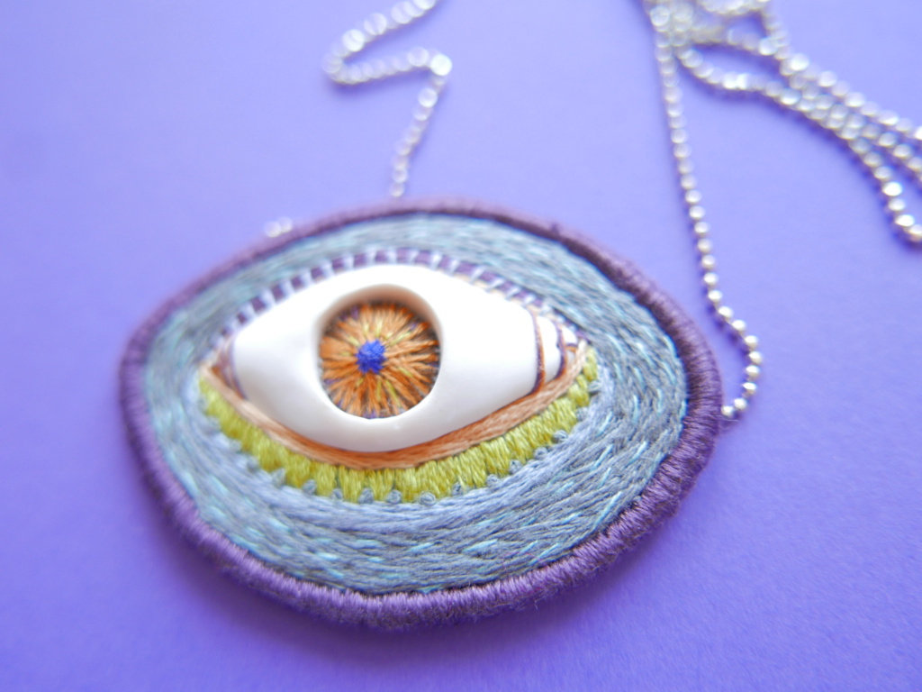 handmade necklace featuring polymer clay eye on a grey background